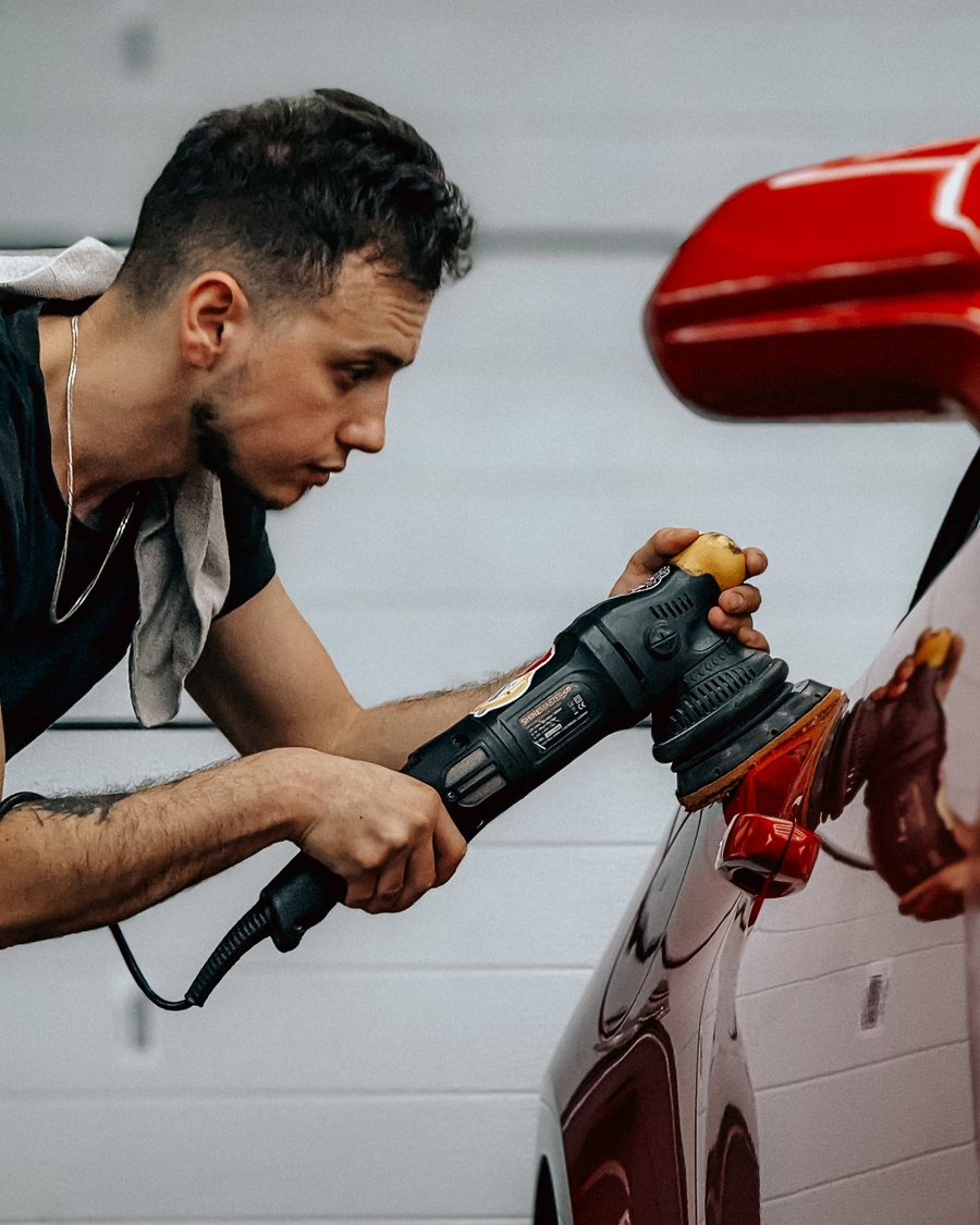 Detailer working a polisher along a red fender
