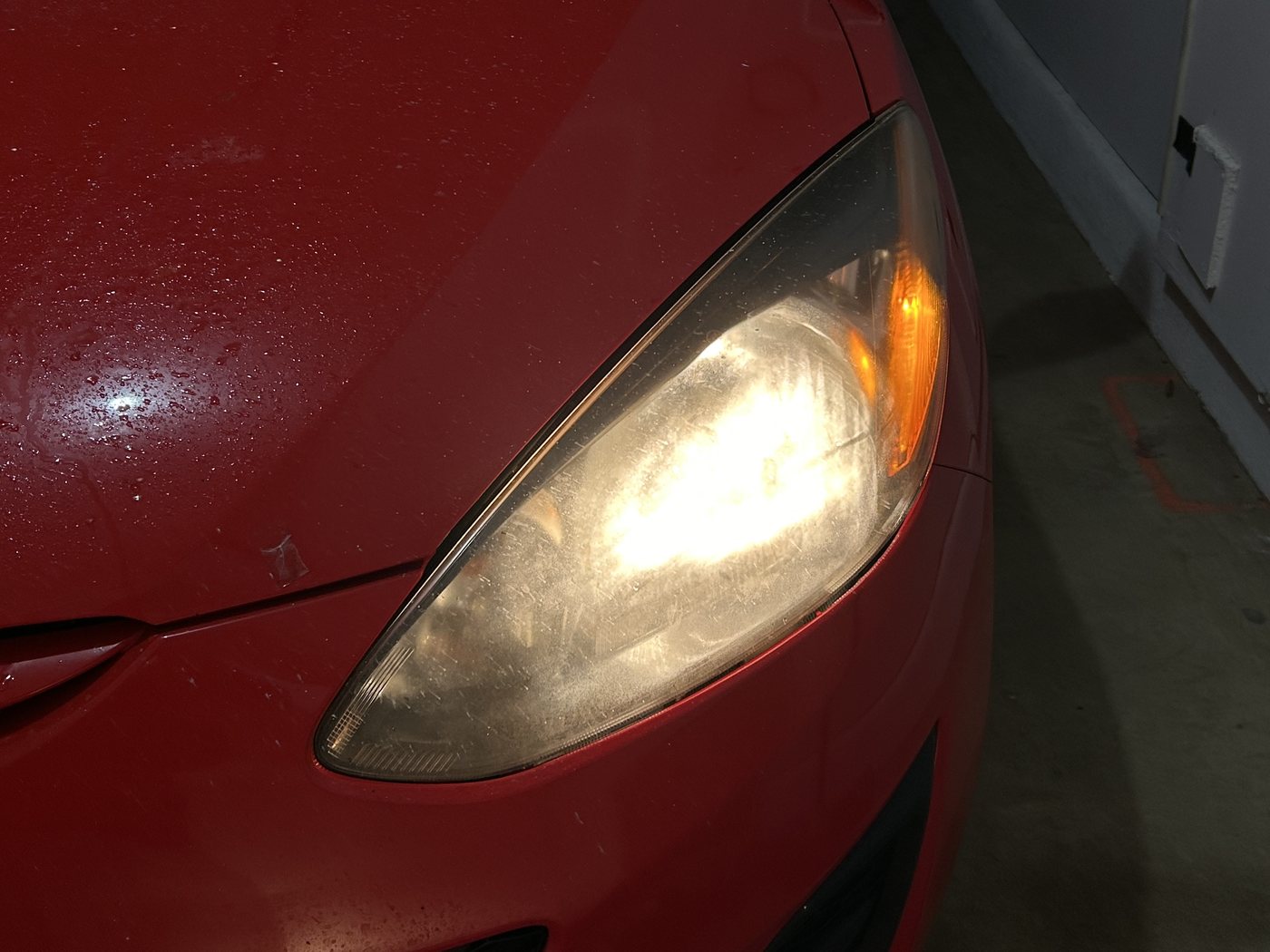 Frosted headlight on a red Mazda 3, the bulb glowing as a milky blur behind the lens