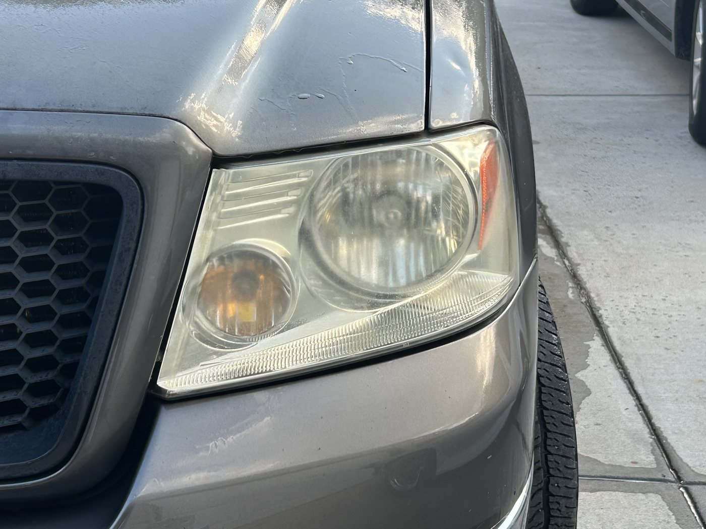 Clouded, yellowed headlight on a silver Ford F-150, the reflector barely visible through the haze